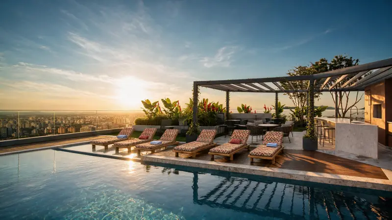 Terraço da cobertura ao pôr do sol, com piscina, espreguiçadeiras estampadas, pergolado com bar e plantas tropicais e guarda-corpo de vidro aberto para a cidade.