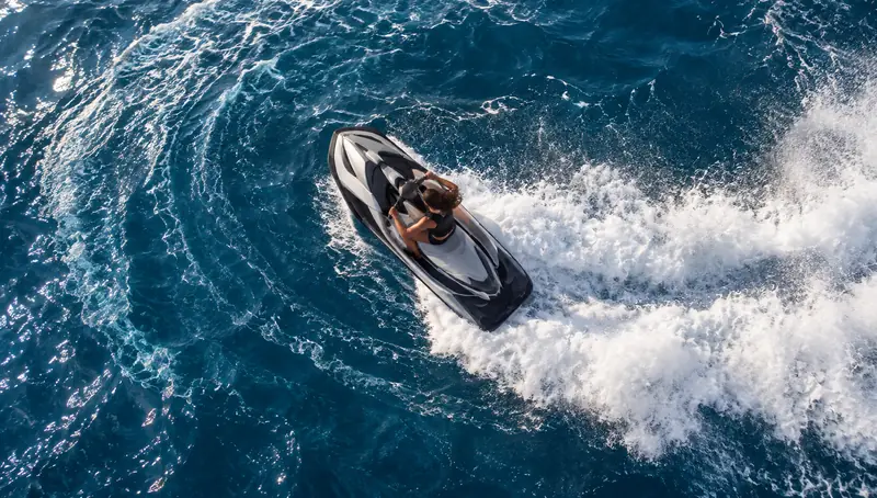 Jet ski visto do alto fazendo uma curva no mar azul-escuro, deixando um rastro largo de espuma branca em espiral.