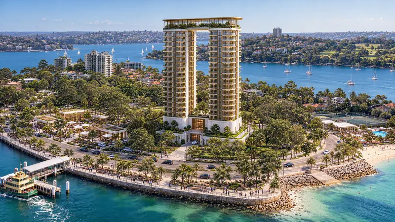 As duas torres unidas pela cobertura vistas de drone em diagonal, com o cais e a balsa em primeiro plano, enrocamento de pedras, praia pequena e a baía cheia de barcos ancorados.
