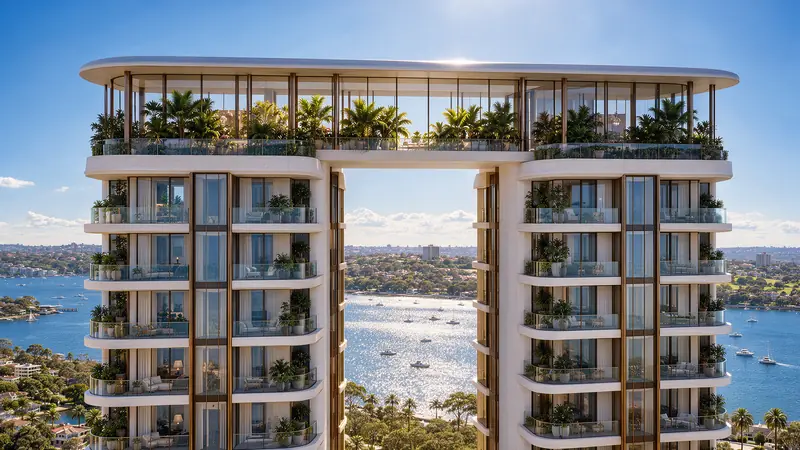 Topo das duas torres ligado por uma cobertura envidraçada com palmeiras e jardim, varandas curvas com plantas e a baía com barcos brilhando ao sol entre os dois volumes.
