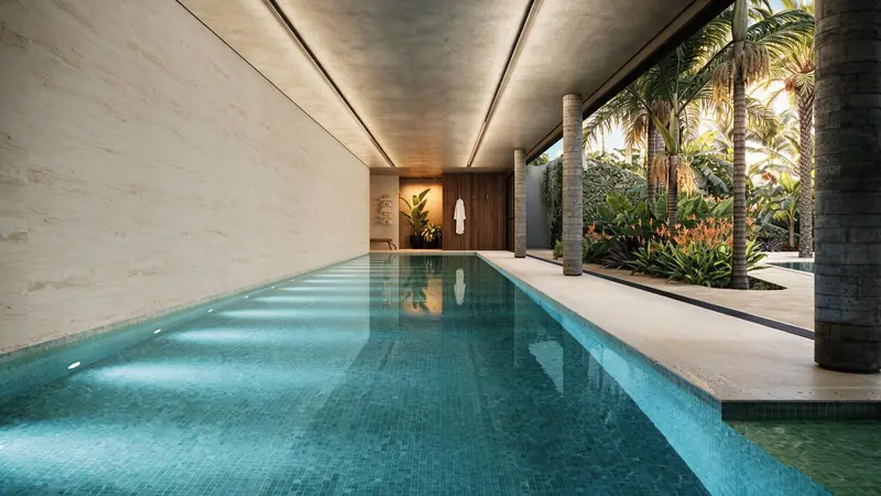 Piscina de raia coberta com pastilhas verdes, parede de travertino, forro com rasgos de luz e lateral aberta entre colunas para jardim tropical com palmeiras.