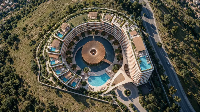 Vista de drone a prumo do conjunto em ferradura sobre o morro, com a cobertura de madeira em leque no centro do pátio, piscinas azuis encaixadas nos terraços e a mata fechada em volta.
