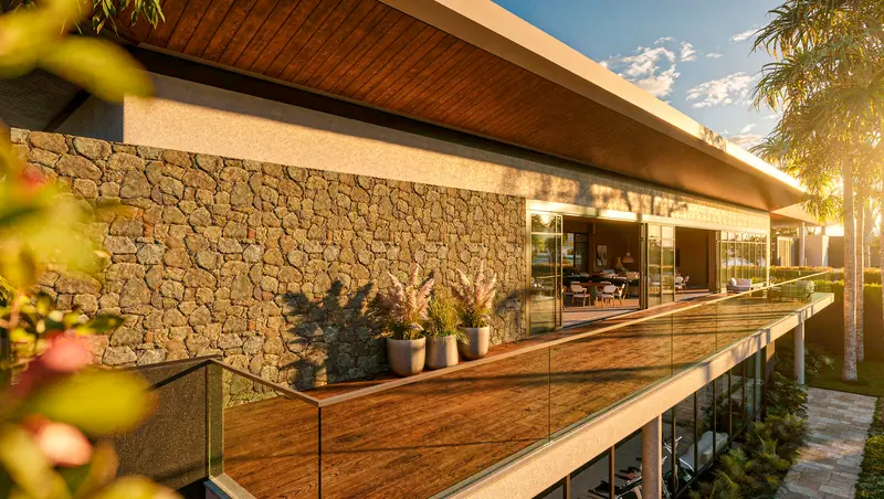 Terraço com deck de madeira e guarda-corpo de vidro ao pôr do sol, parede de pedra, vasos com capim-dos-pampas, beiral de madeira e salão envidraçado ao fundo.