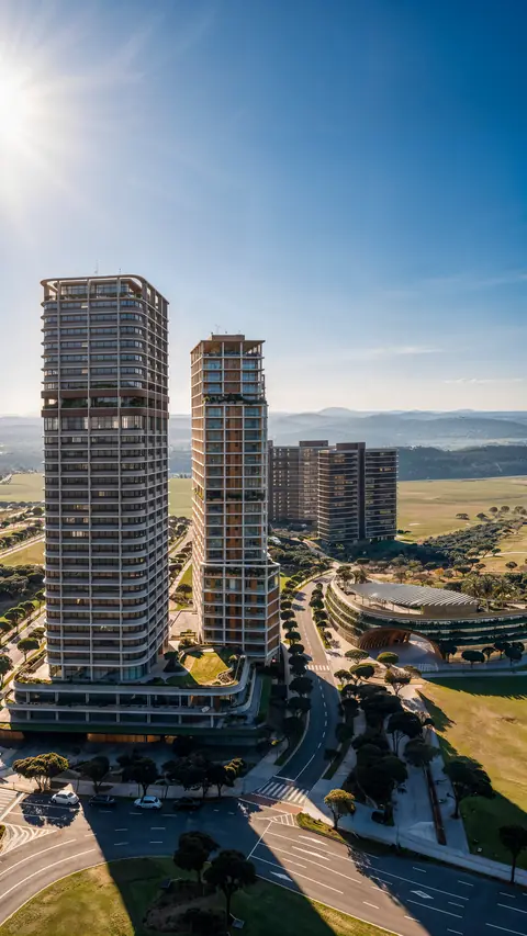 Duas torres de faixas horizontais vistas do alto em dia claro, com avenida arborizada, edifício circular baixo, campos abertos e serras ao fundo.